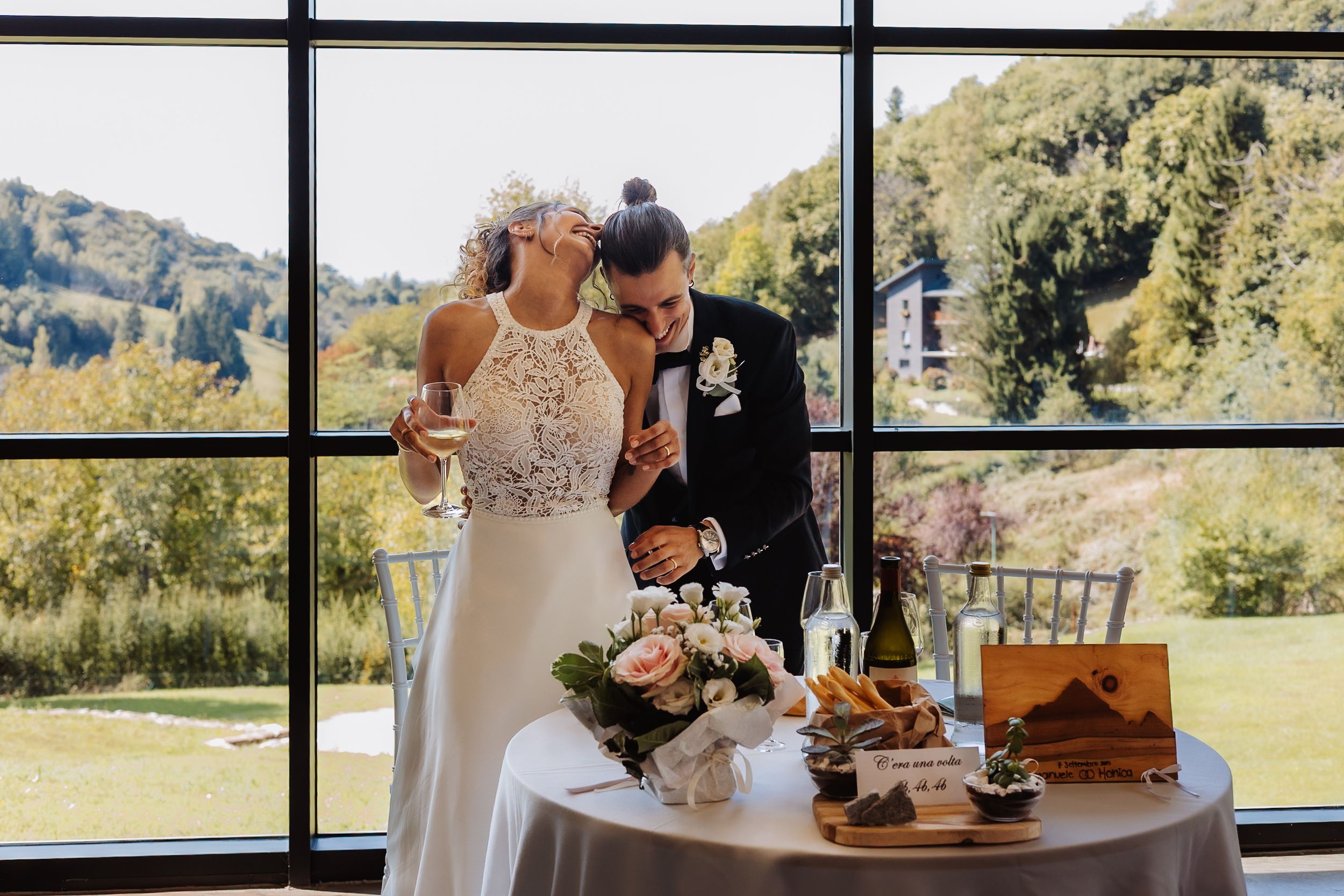Wedding guests gather on a sunny outdoor patio surrounded by scenic mountain views during a reception celebration.