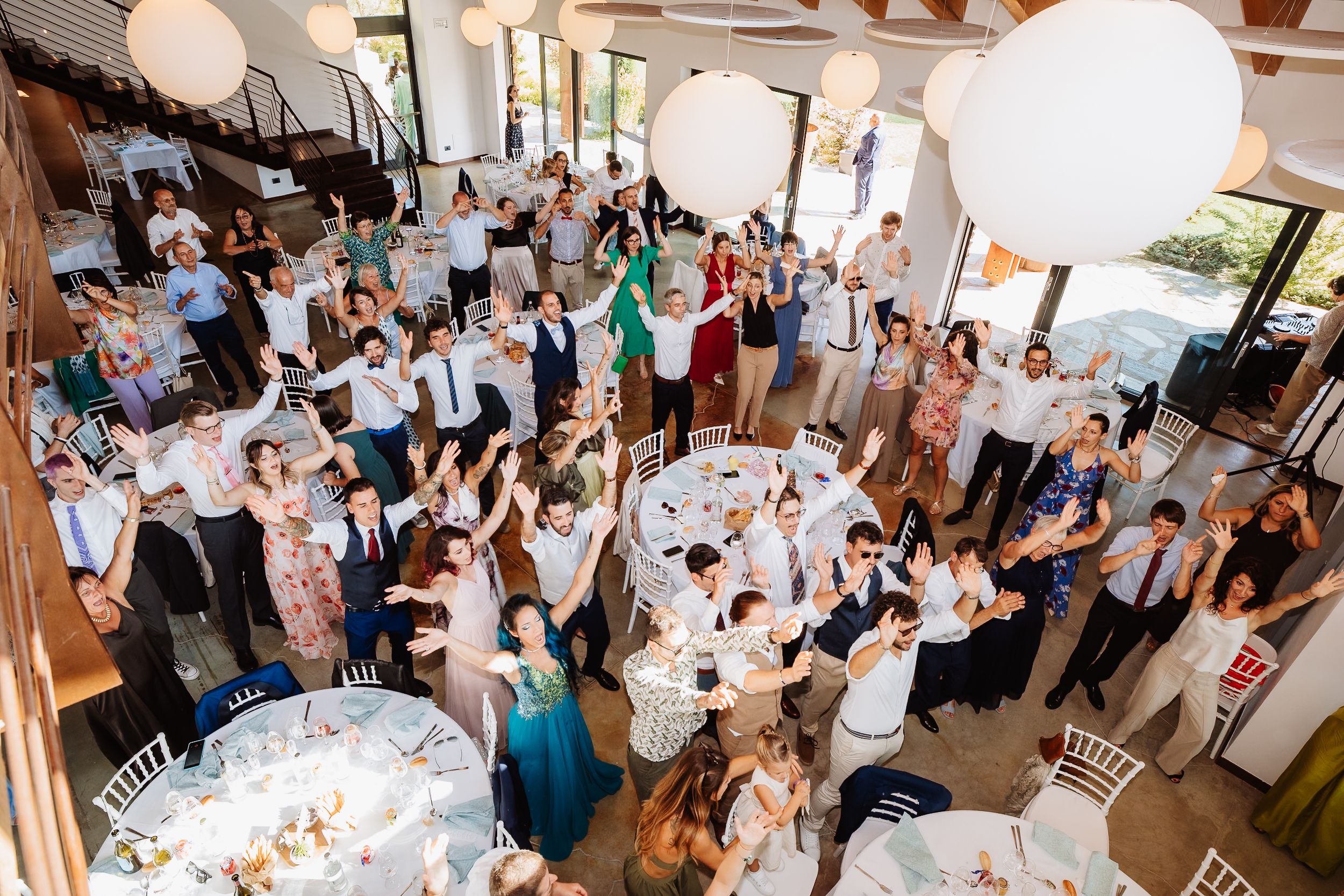 Wedding guests raise their glasses in celebration during a reception toast at a rustic indoor venue.