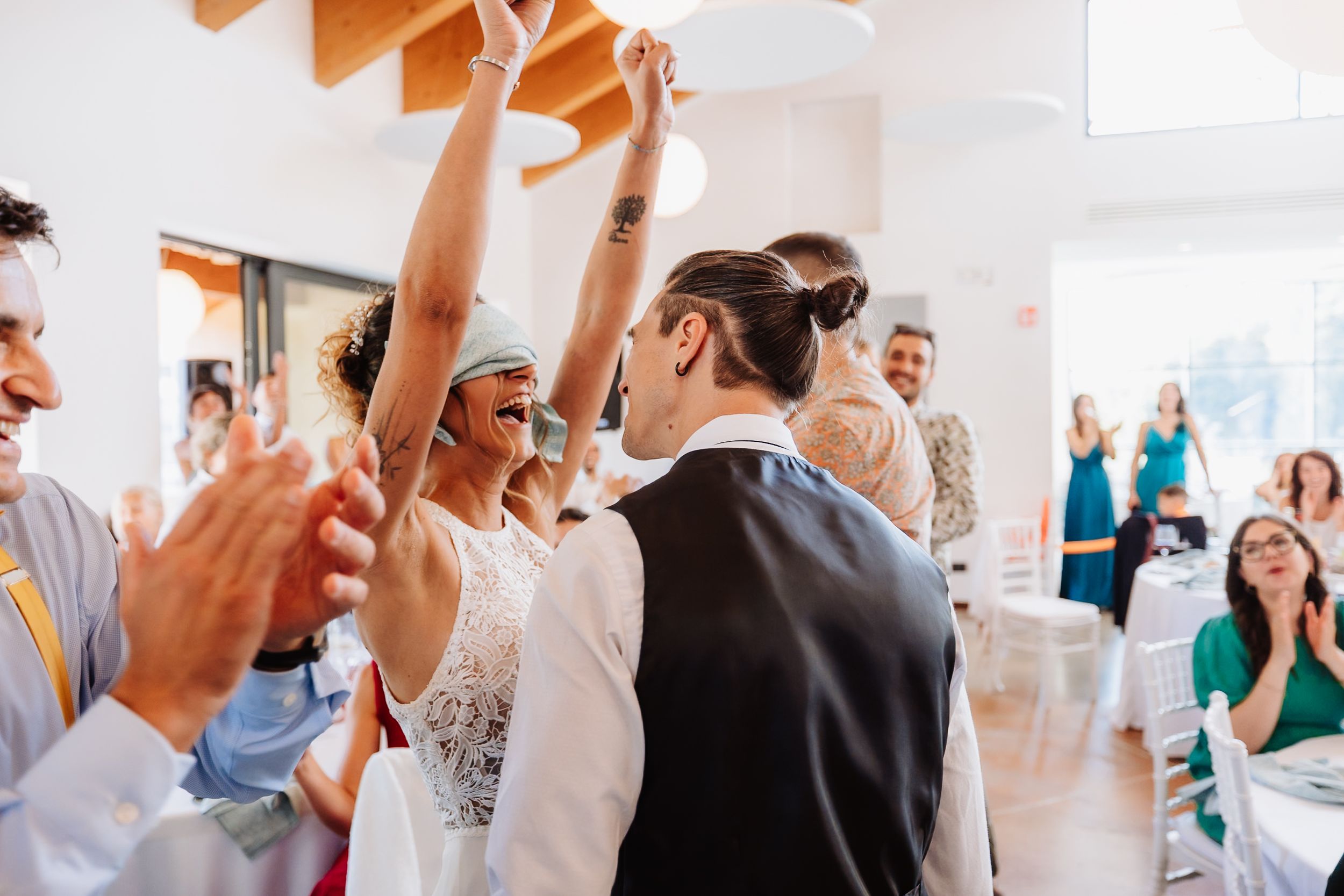 A group of people celebrate and dance together at a wedding reception in a bright indoor venue.