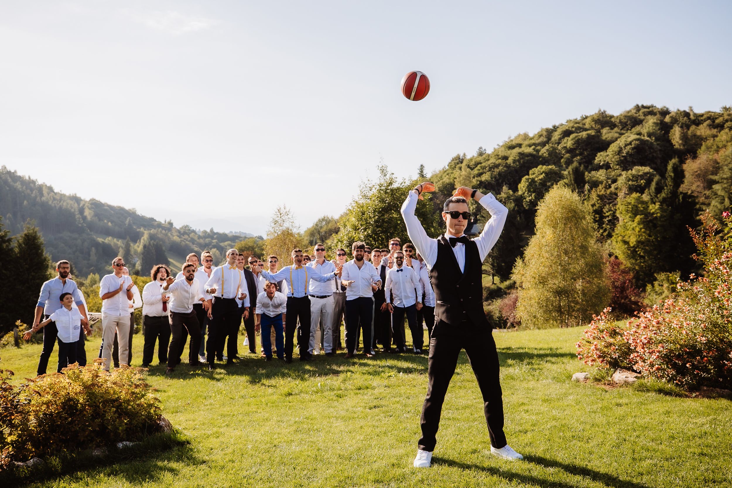 A group of people playing baseball in a scenic mountain meadow on a sunny autumn day.