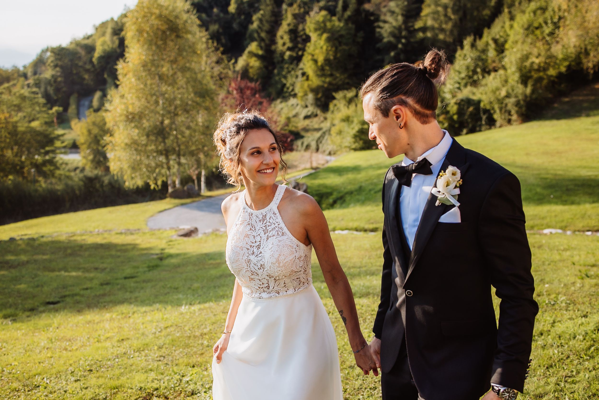A couple shares a romantic moment in a sunlit meadow wearing formal wedding attire.