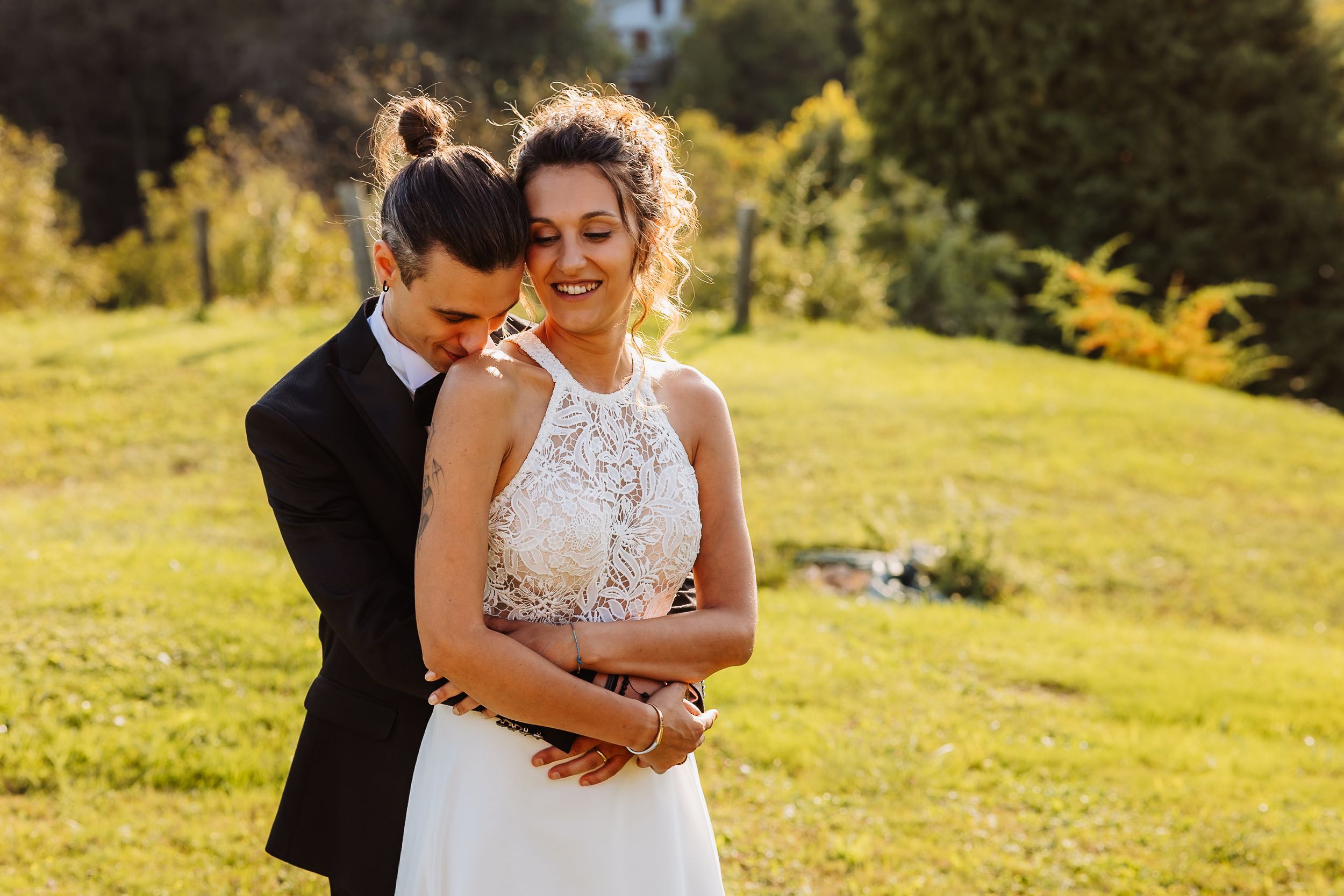 A couple embraces on a sunny hillside during their outdoor wedding celebration.