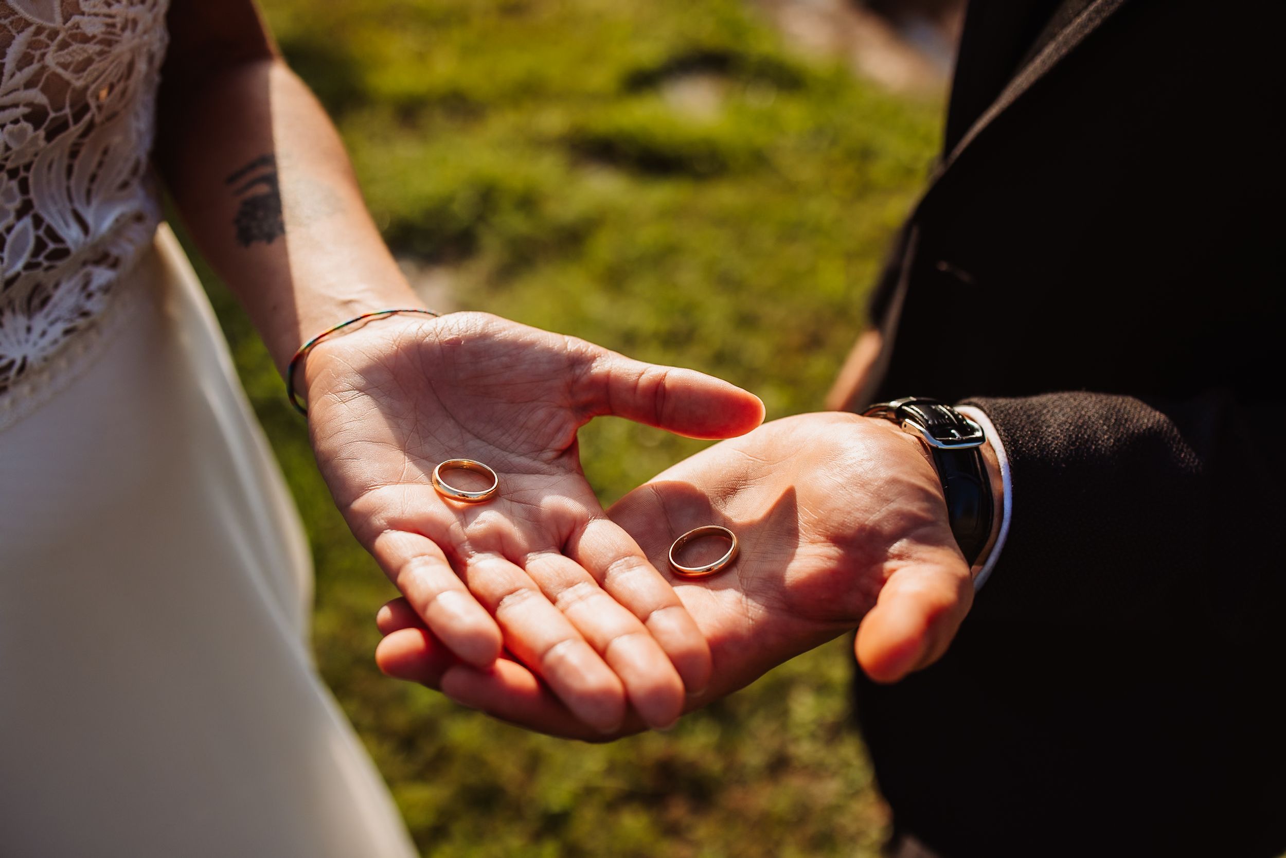 Wedding rings held in open palms during outdoor ceremony with sunlit grass in background.