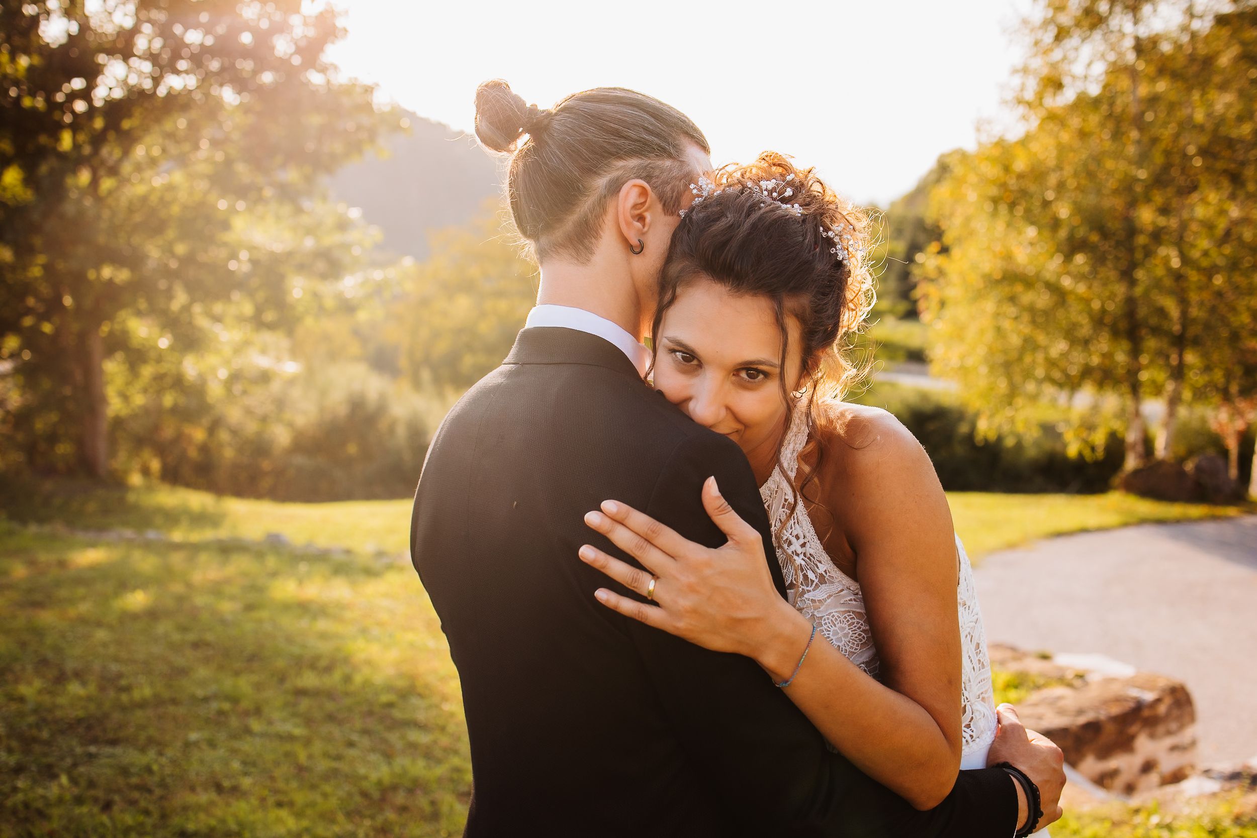 Romantic couple embraces in golden sunlight during sunset photoshoot in a scenic outdoor setting.