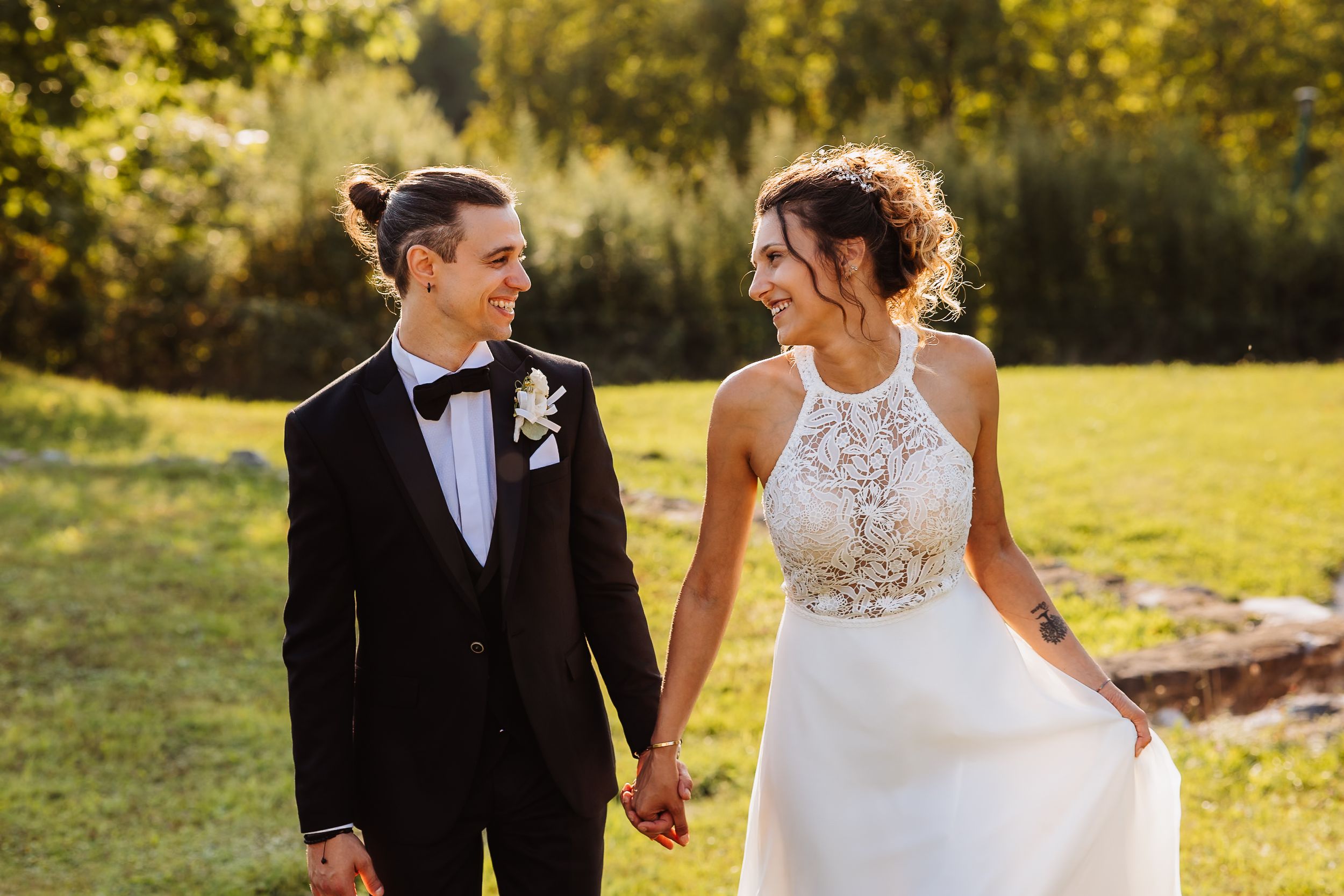 A romantic wedding couple walks hand in hand through a sunlit autumn field during golden hour.