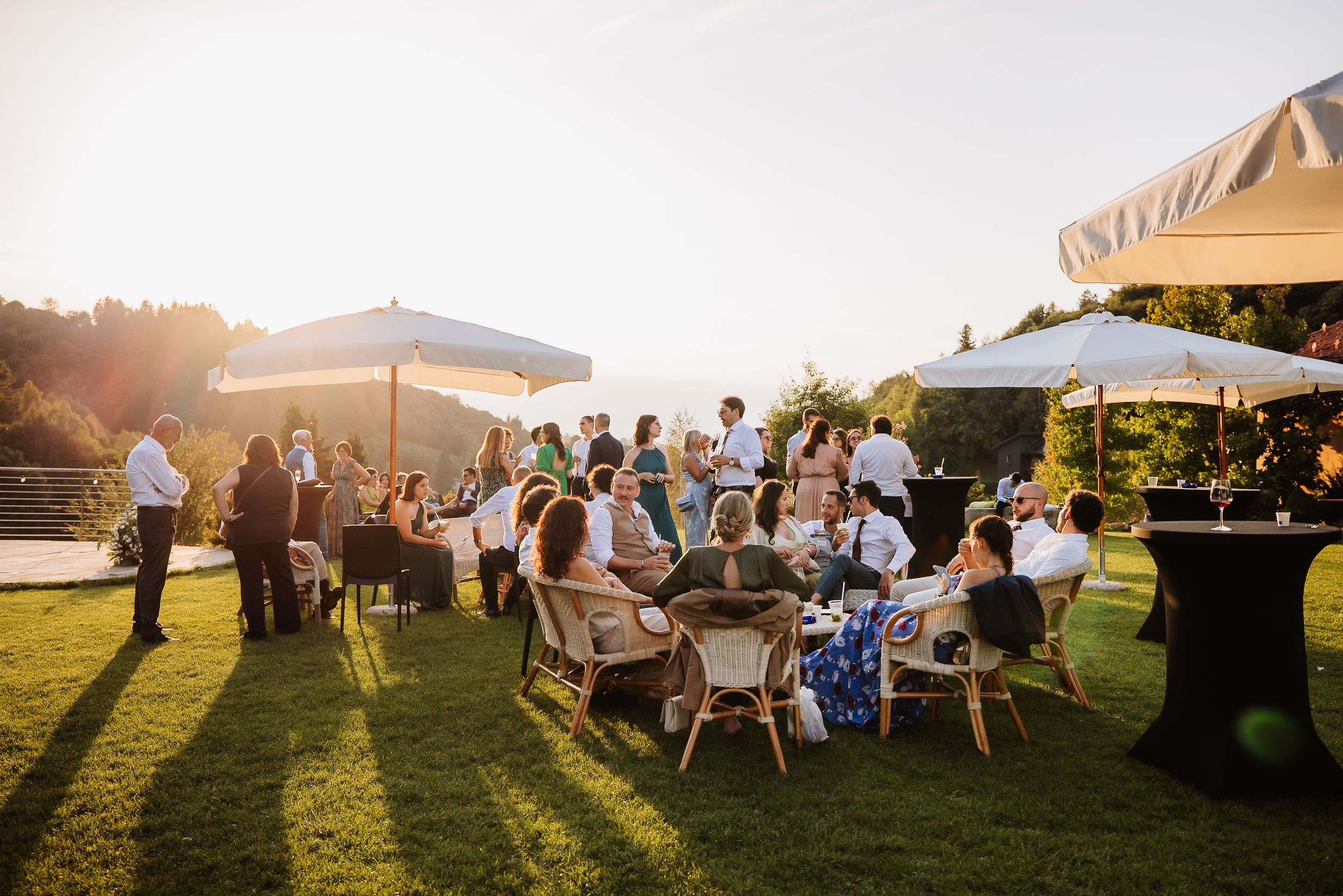 Wedding guests enjoy an outdoor reception under white tents at sunset with mountain views in the background.