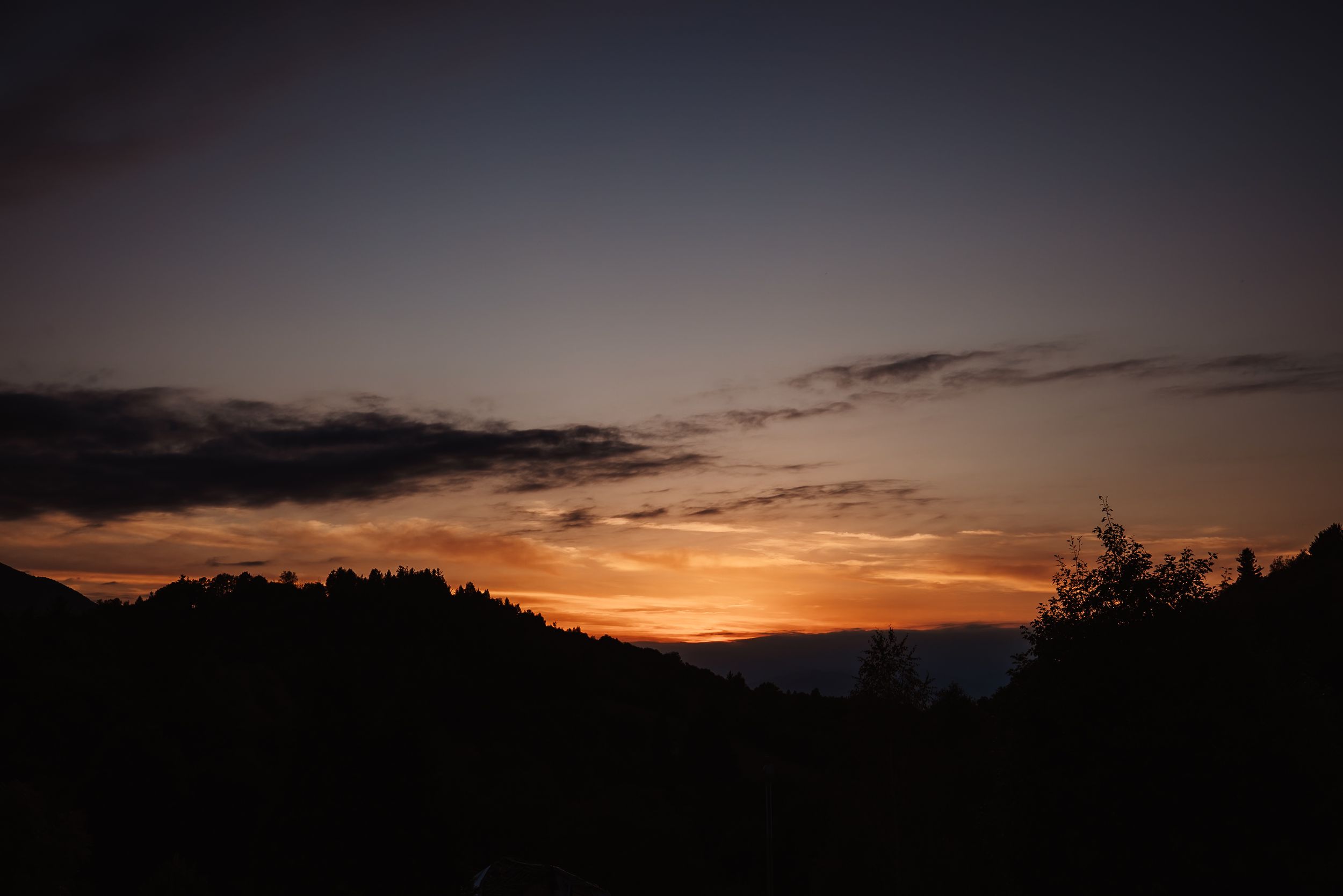 Dramatic orange sunset sky over dark mountain silhouettes with wispy clouds during dusk.