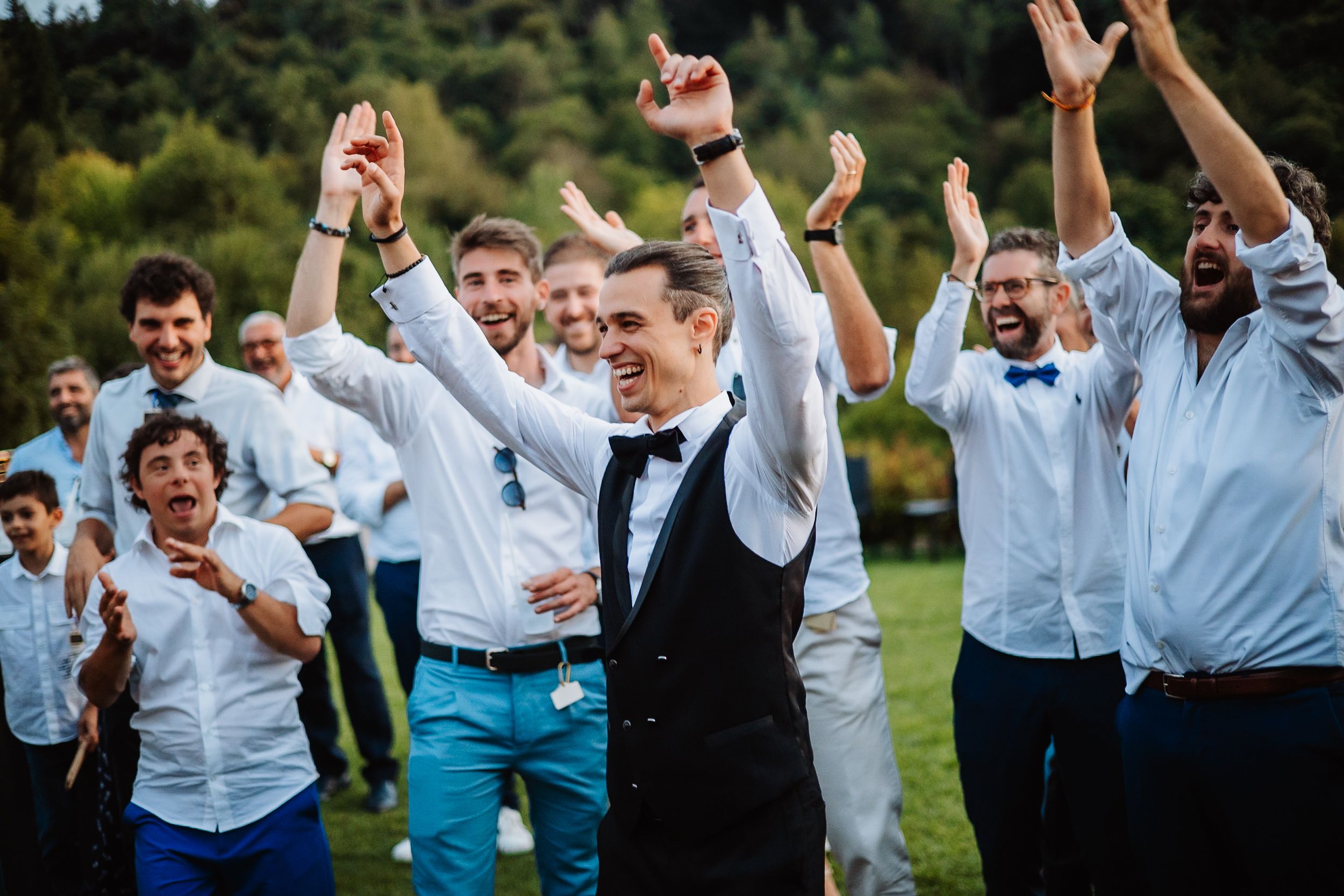 Wedding party in blue and white attire jumping joyfully in an outdoor garden setting.