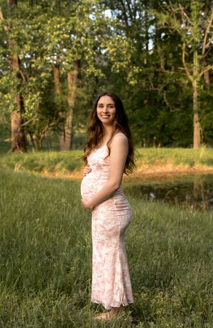 Maternity portrait session in a grassy field with trees and natural lighting.