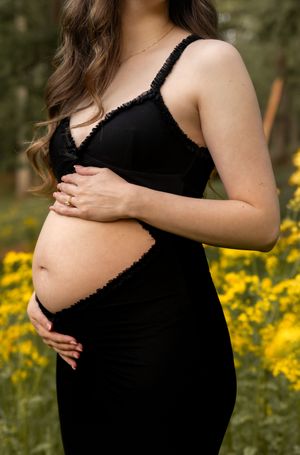 Intimate maternity portraits in black dress surrounded by bright yellow wildflowers.