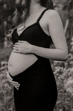A black and white maternity portrait showing a tender moment with hands cradling the baby bump.