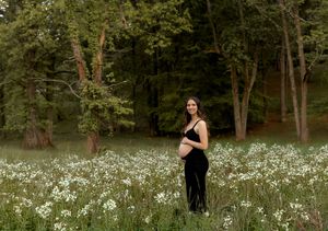 Spring maternity session in meadow with white wildflowers and green grass.