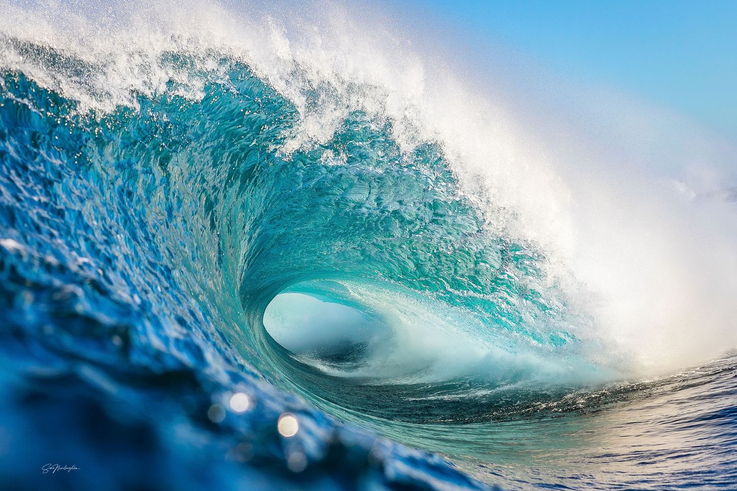 Powerful ocean wave creates a crystal blue barrel formation as it crashes towards the shore.