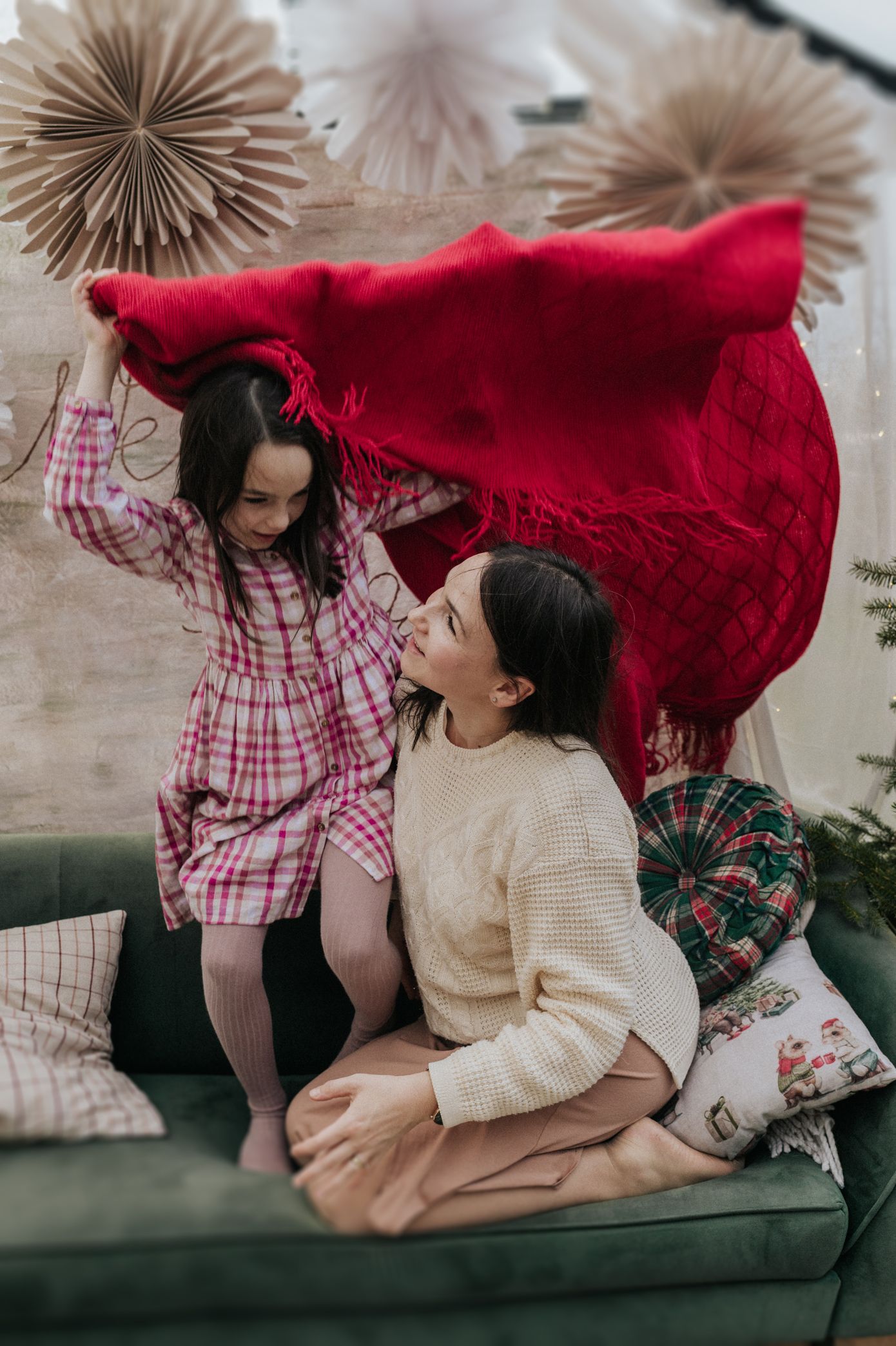 Two people share playful moments on a green couch with decorative paper fans on the wall behind them.