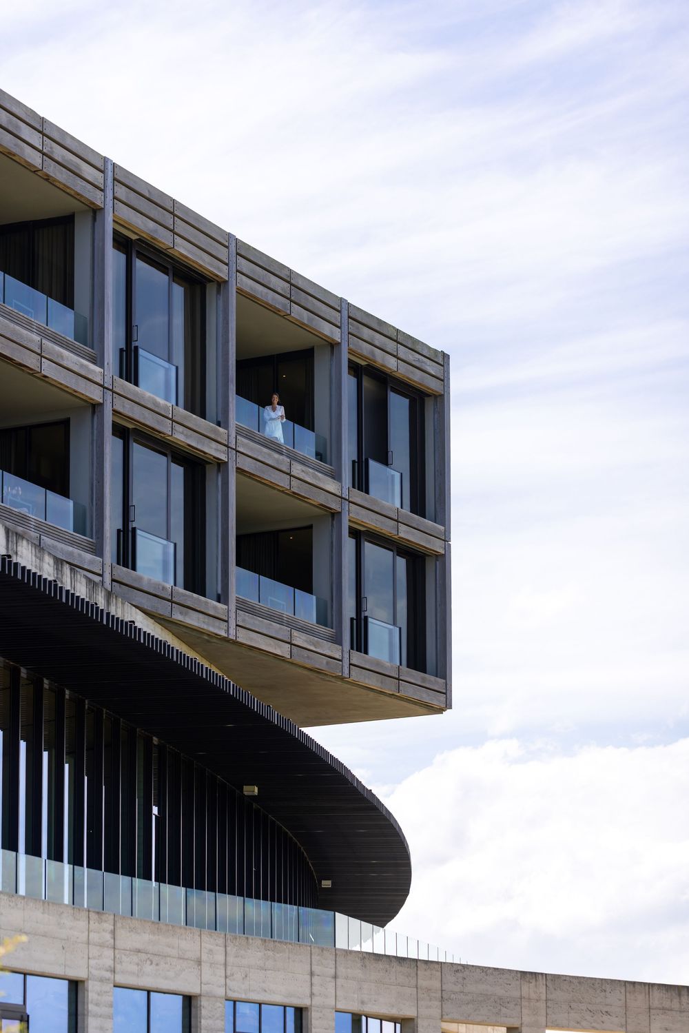Modern office building with curved architectural details and glass balconies against a cloudy sky.