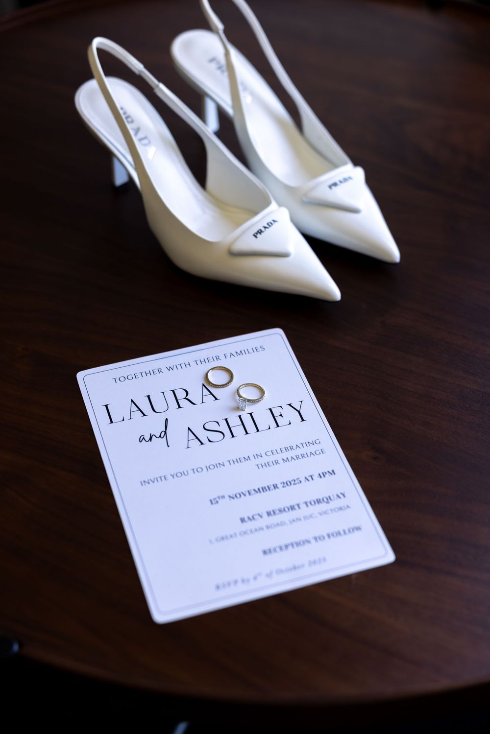 White bridal shoes and elegant wedding invitation displayed on dark wooden surface.