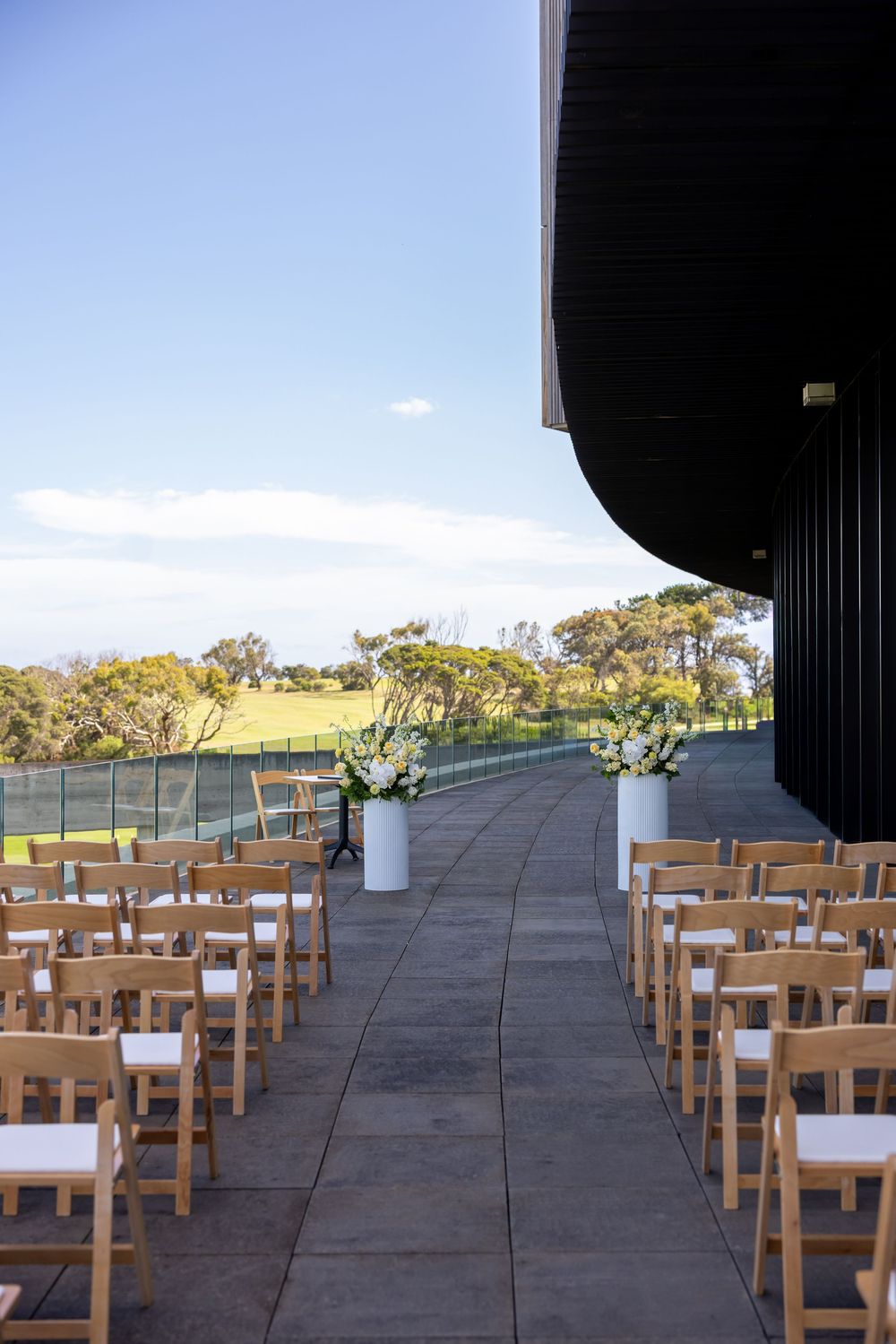 Outdoor wedding ceremony setup with wooden chairs arranged in rows on a patio overlooking scenic countryside views.