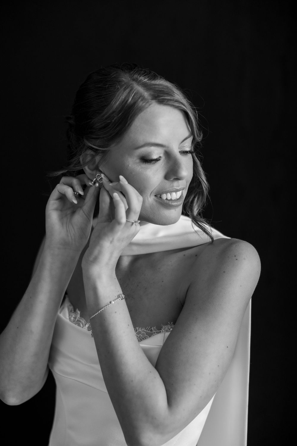 Black and white portrait of someone wearing a white dress and jewelry while smiling with eyes closed.