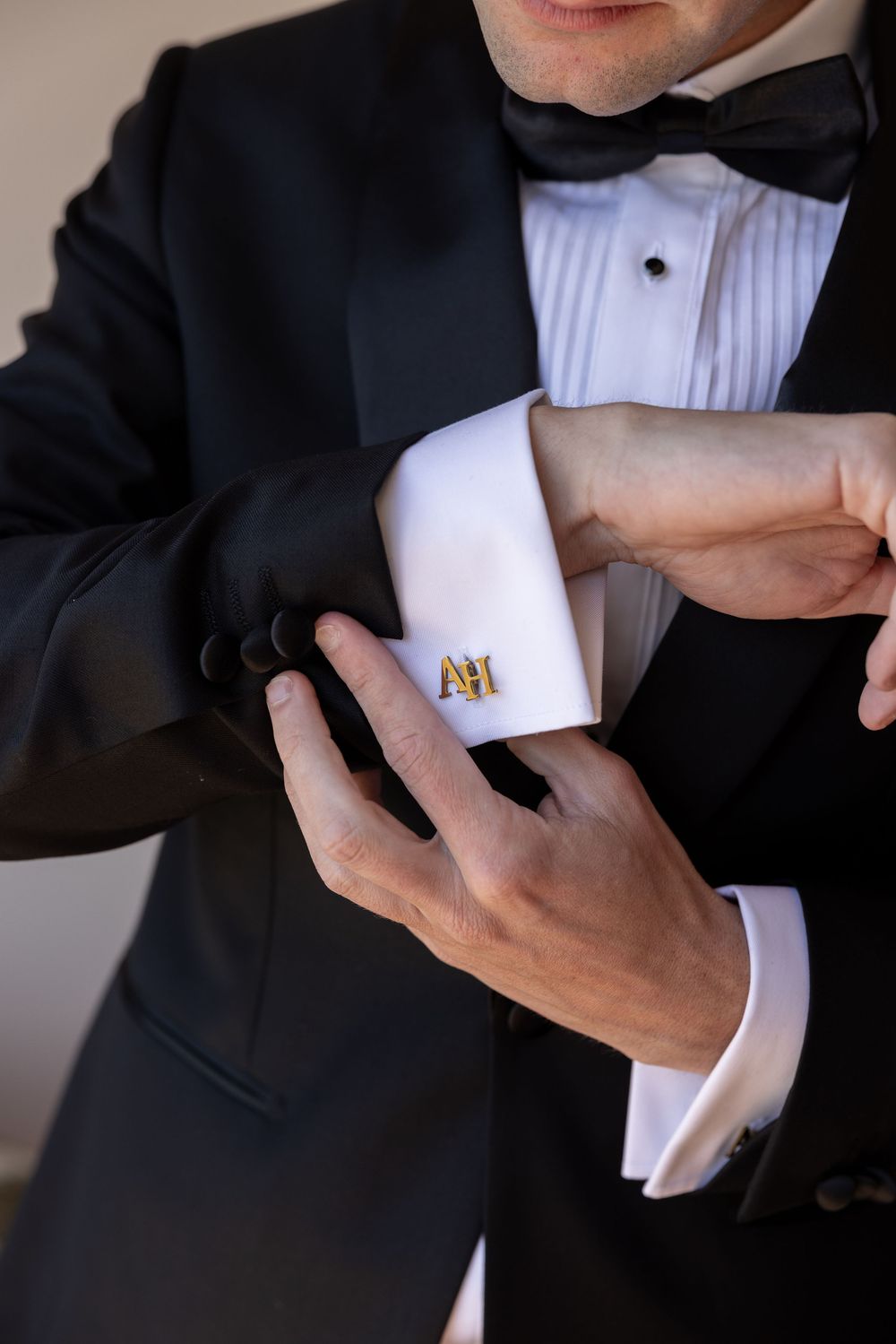 Close-up shots of adjusting formal black tuxedo cuffs with gold monogrammed cufflinks.