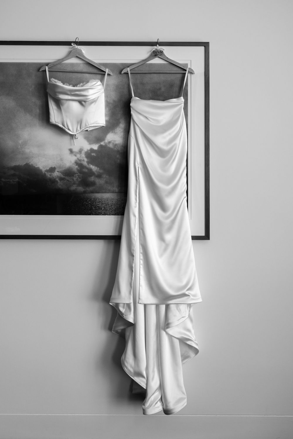 A series of black and white photographs showing a white wedding dress hanging on display against different wall backgrounds.