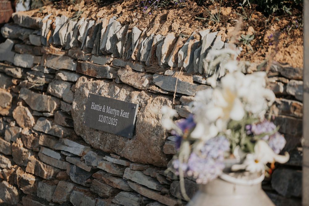 Rustic stone wall with a personalized slate wedding plaque and elegant white floral arrangement.