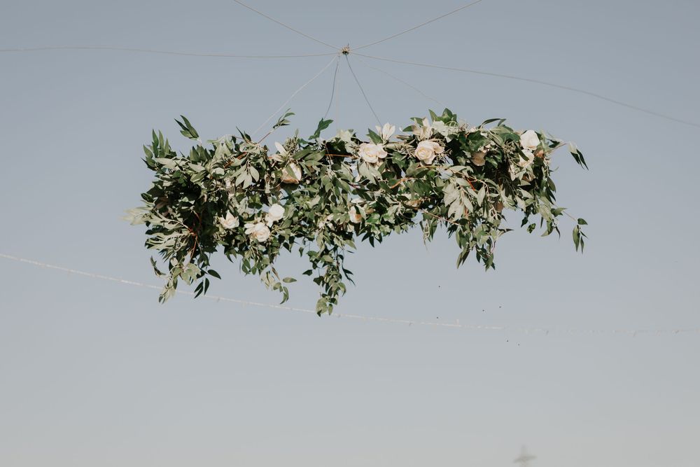 Stunning suspended floral installation with greenery and white roses hanging against a clear blue sky.