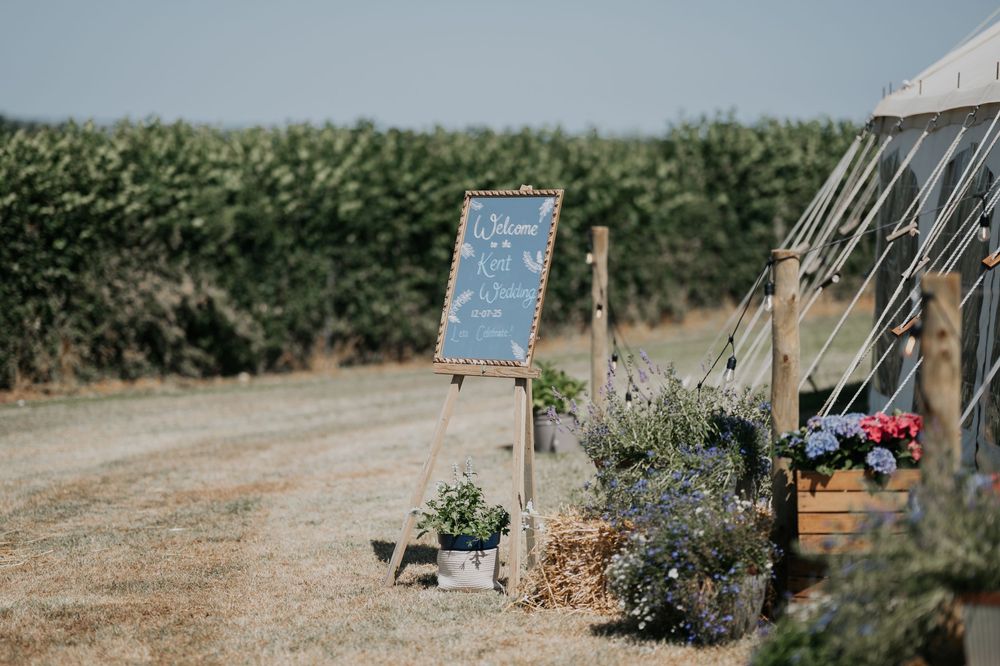 Rustic outdoor wedding welcome chalkboard sign with lavender and flowers beside a white bell tent.