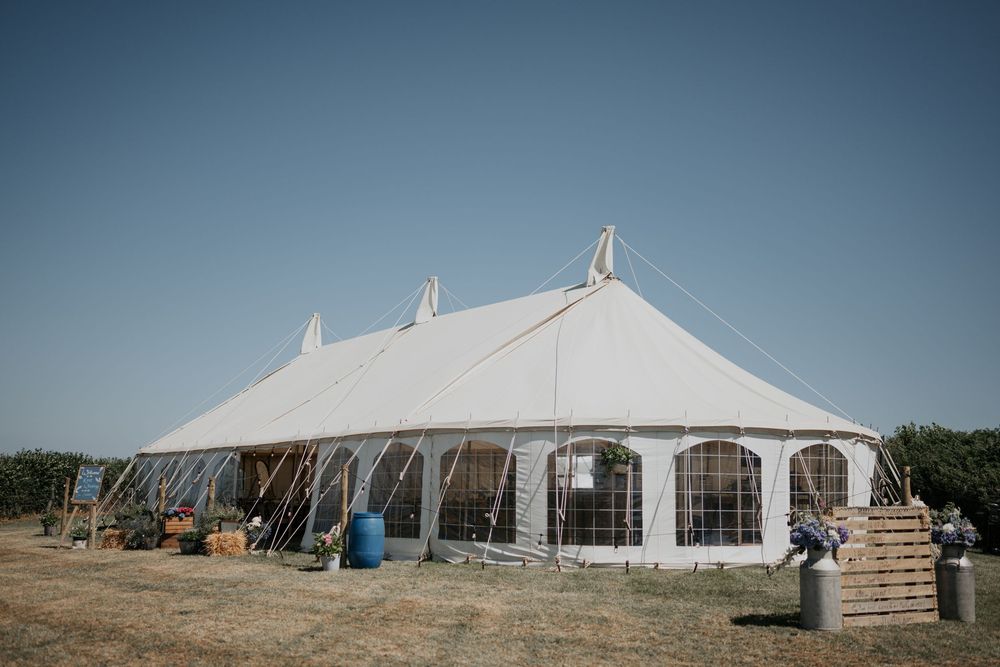 Large white traditional pole marquee tent set in an open field under a clear blue summer sky.