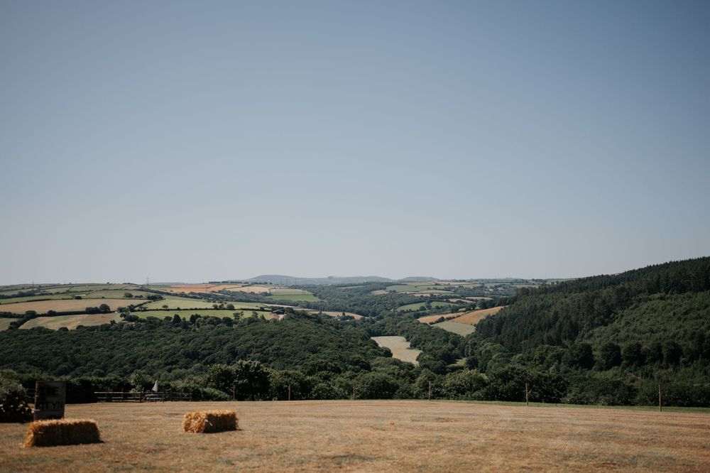 Scenic countryside wedding venue with golden hay bales and rolling green hills under a clear blue sky.