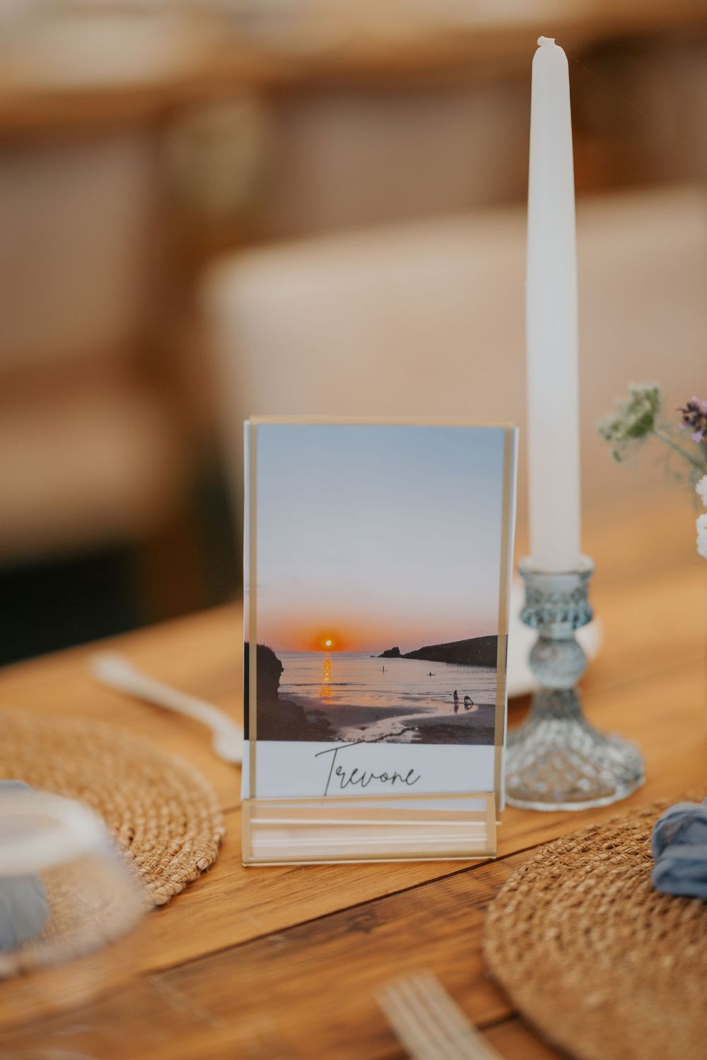 Wedding table number featuring a sunset beach photo in a gold frame beside a white taper candle.