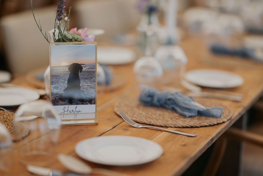 Coastal wedding table setting with a photo centerpiece, blue napkins, and wildflower arrangements.
