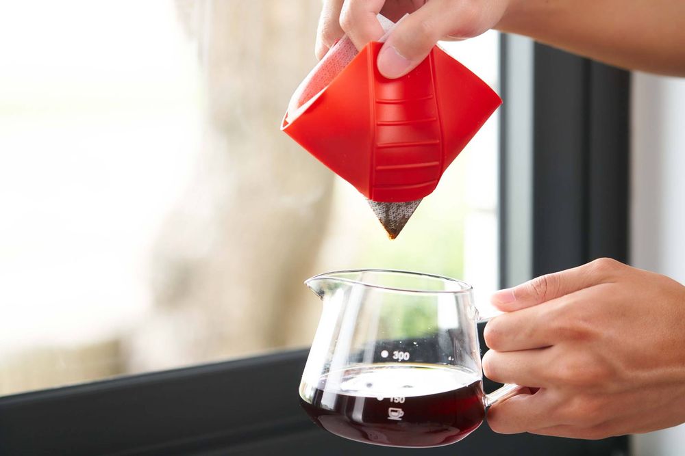 Hands pour red wine from a decanter into a glass while natural light streams through a window.