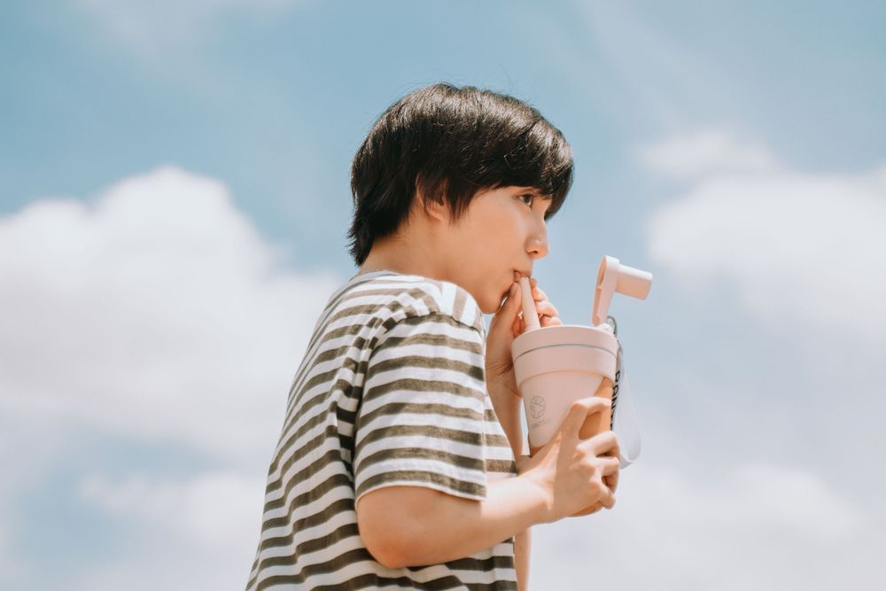A child in a striped shirt sits on a bench against a cloudy sky background.