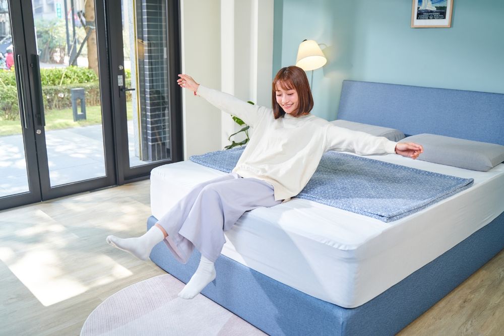 Person demonstrating proper bed making technique with white linens and pillows in a bright modern bedroom.