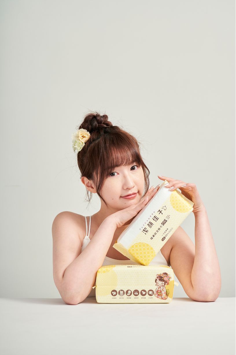 A person lying on a white surface poses playfully with yellow decorative items in a minimalist studio setting.