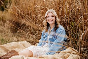 Person in light blue denim jacket sits in golden grass field during autumn sunset photoshoot.