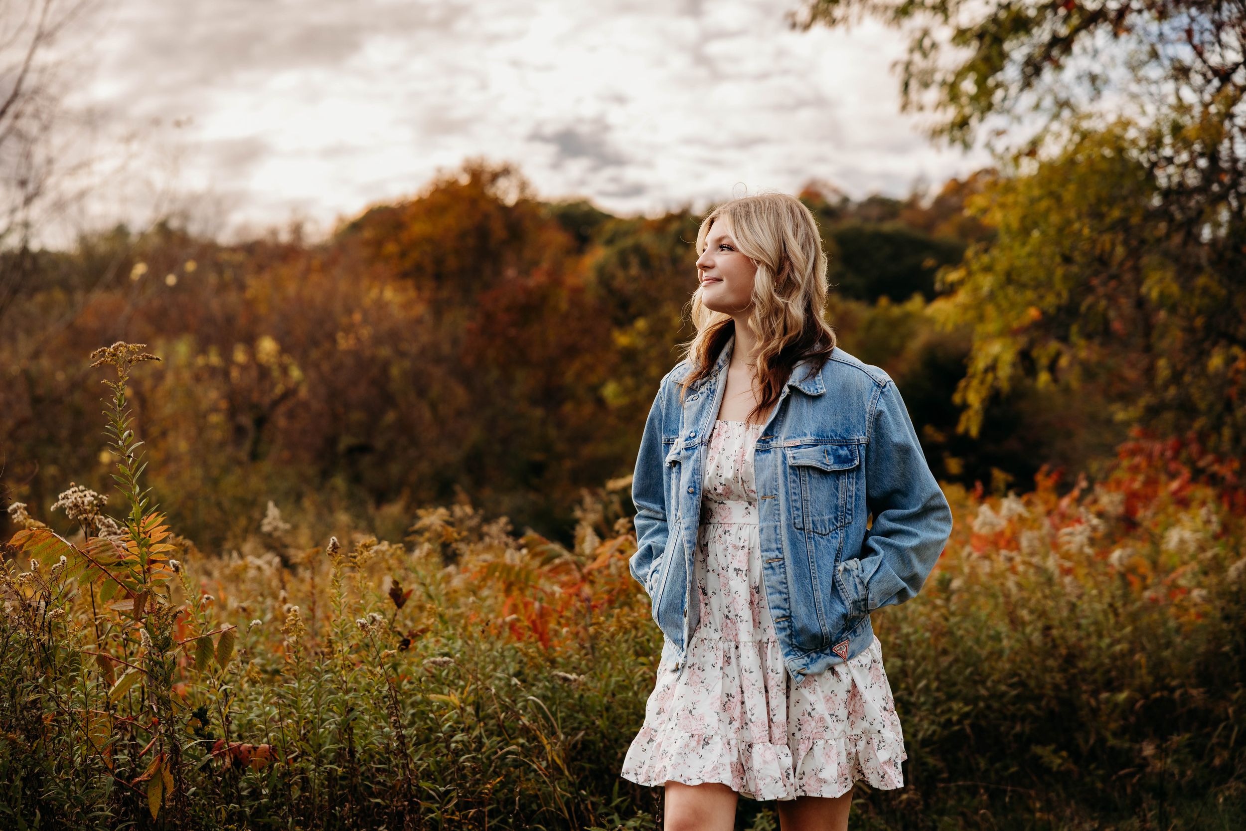 Autumn outdoor scene with denim jacket and floral dress against colorful fall foliage in golden sunlight.