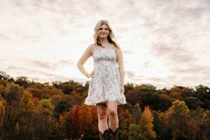 A scenic autumn photoshoot in a park with colorful fall foliage and a white lace dress against the sunset sky.