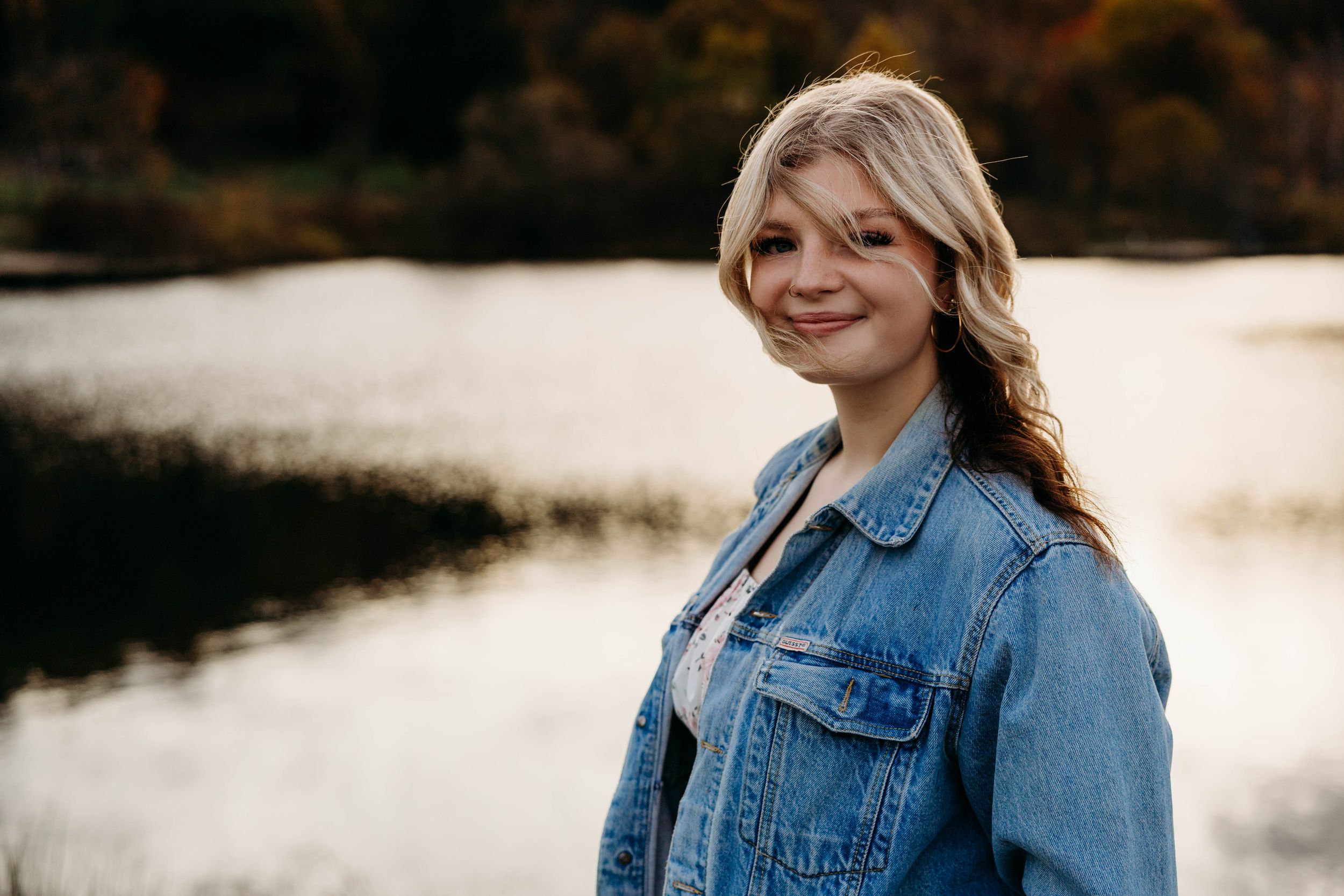 A woman in a denim jacket stands outdoors at sunset with golden light creating a warm, dreamy atmosphere.