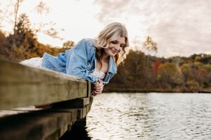 Couple enjoying a romantic autumn engagement photoshoot by a serene lake at sunset.