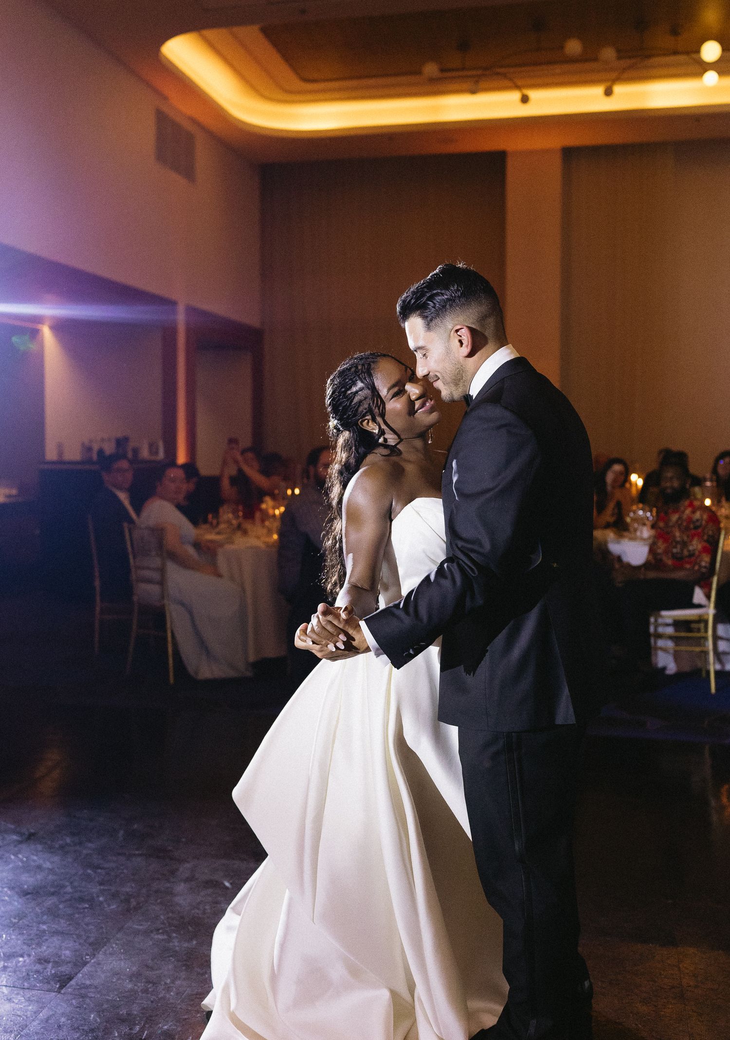 Interracial couple sharing joyful first dance at elegant wedding reception venue.