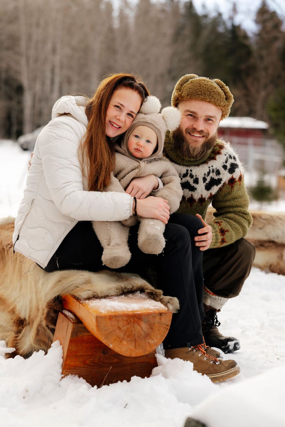 A family plays together in the winter snow while sitting on a wooden sled in a snowy forest landscape.