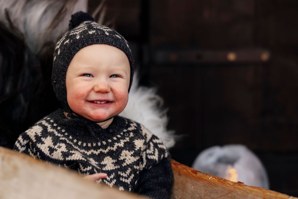 A child wearing a black and white patterned knit hat smiles warmly in a dark indoor setting.