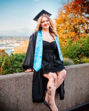 Girl sits on stone wall in cap and gown.