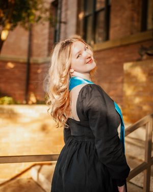 Graduate celebrates on stairs in sunlight backdrop.
