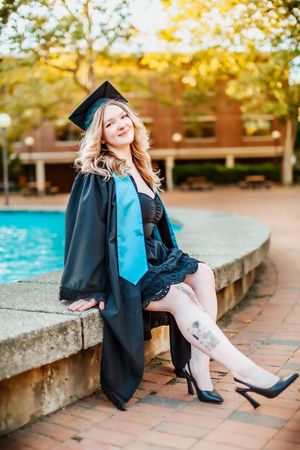 Graduate poses in front of fisher fountain.