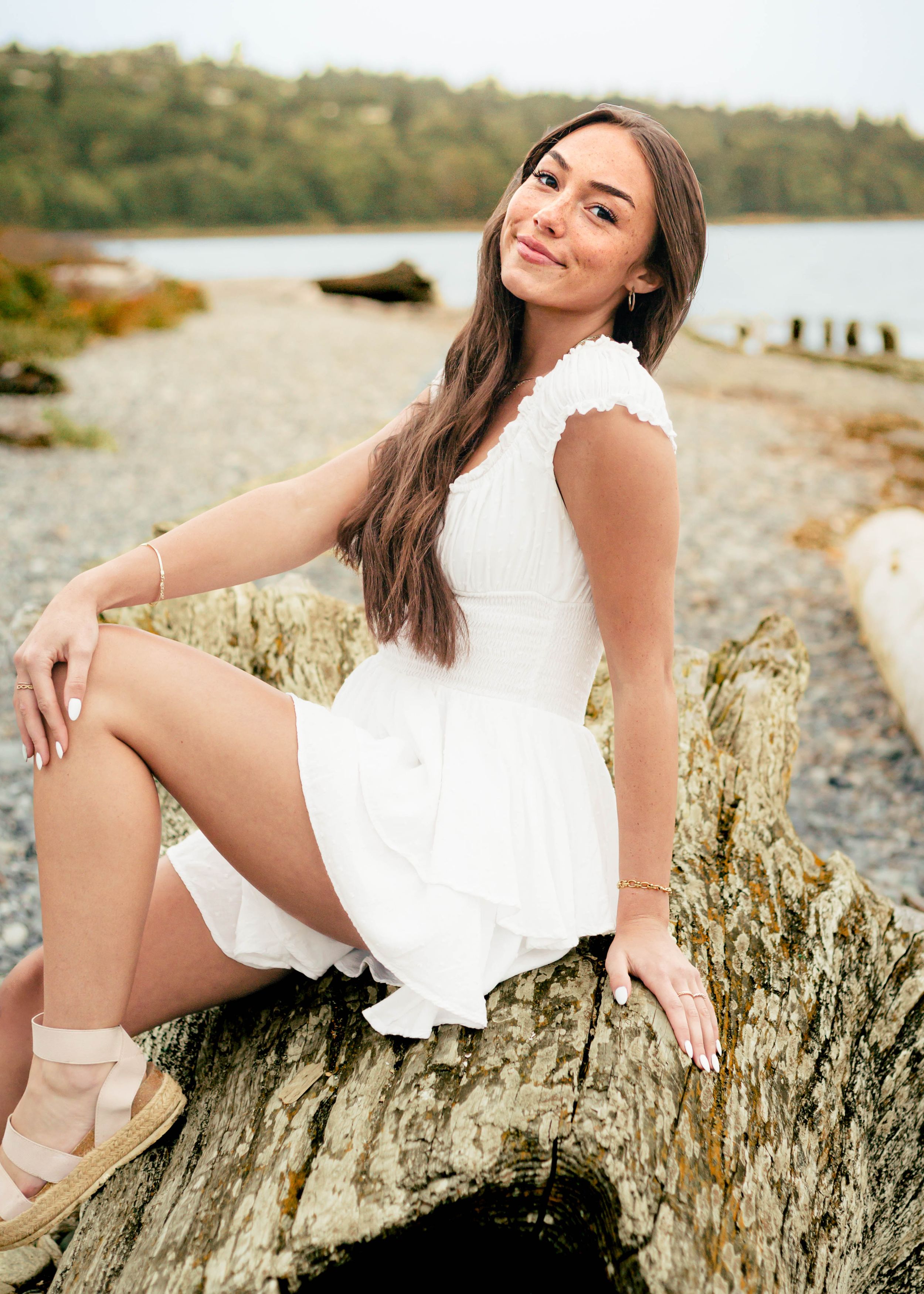 Girl sits on log on beach overlooking the coast of the pacific north west.
