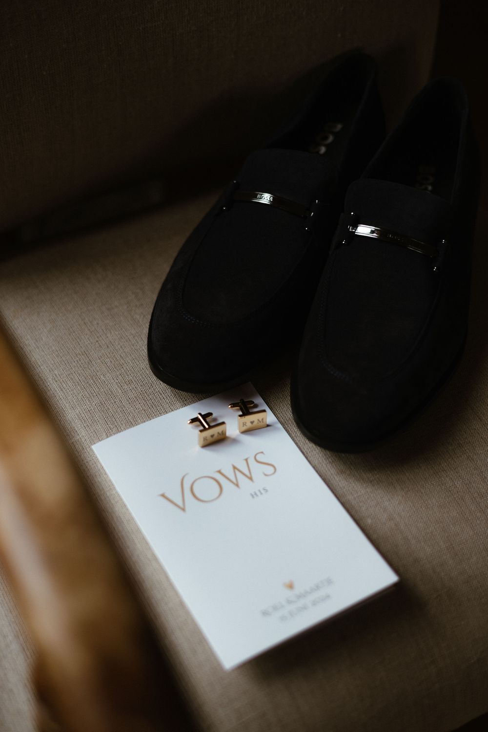 Wedding vows booklet with cufflinks and formal shoes in moody lighting.