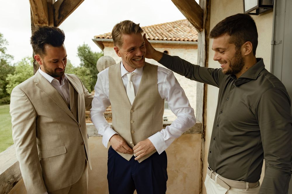 Wedding party members in light suits sharing laughs on covered porch.