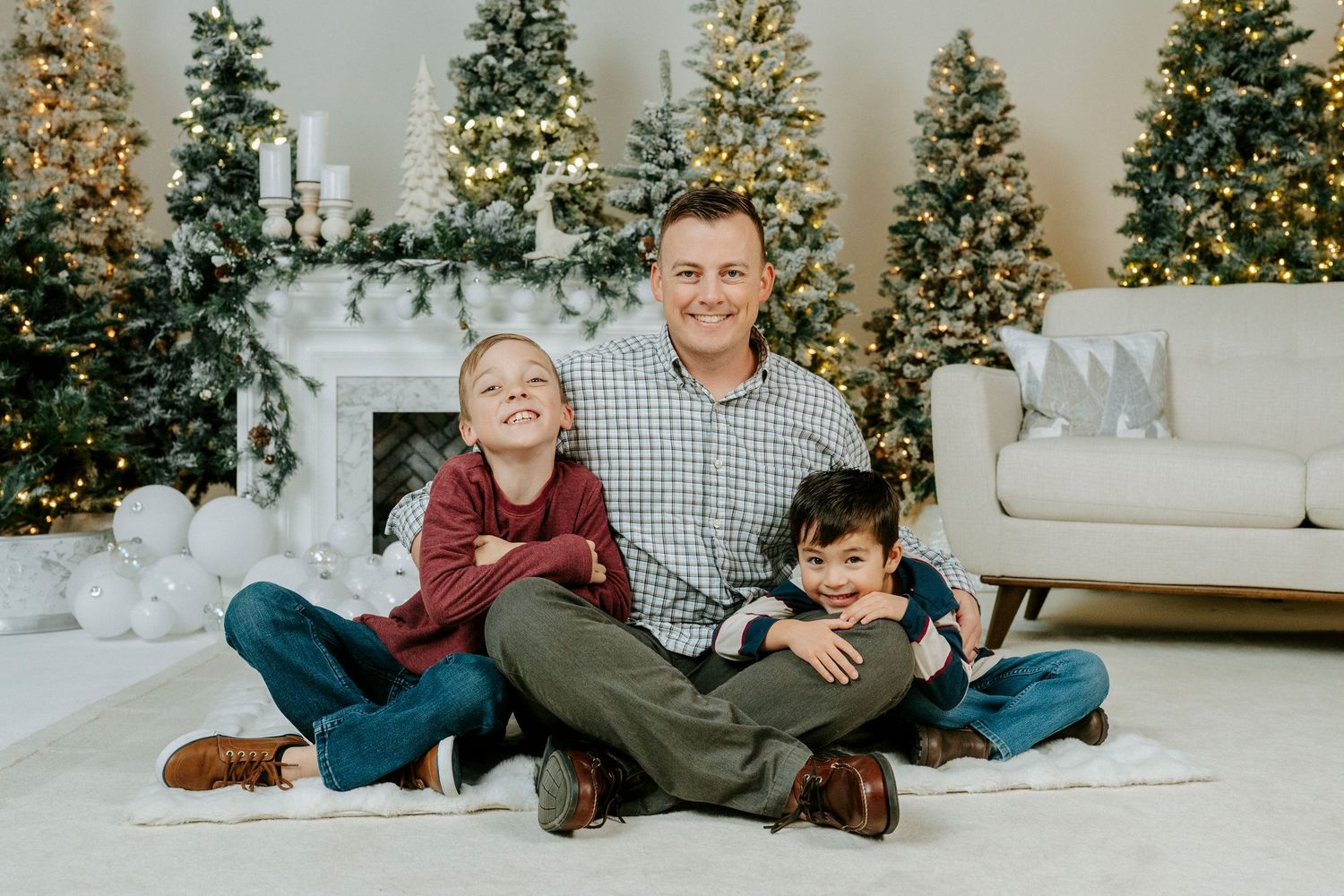 Family poses together on white carpet in front of decorated Christmas trees in living room for holiday photos.